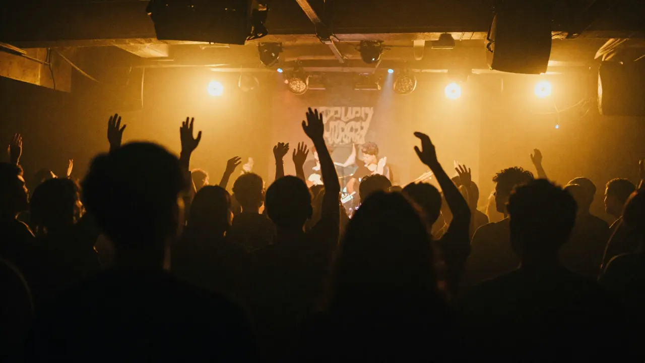 Crowd with raised hands in front of yellow stage lights at an indie gig in a dark club